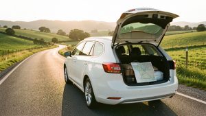 Voiture familiale roulant sur une route estivale ensoleillée, avec des valises discrètes et une carte routière aux lignes abstraites.