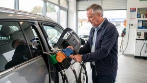 Un conducteur compare trois pistolets de carburant près de la trappe ouverte d’une voiture essence dans une station-service française.