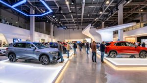 Vue dynamique d’un salon automobile au Parc Expo de Tours, avec des voitures neuves et des SUV éclairés sur des stands modernes, tandis que des visiteurs comparent les habitacles.