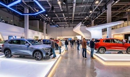 Vue dynamique d’un salon automobile au Parc Expo de Tours, avec des voitures neuves et des SUV éclairés sur des stands modernes, tandis que des visiteurs comparent les habitacles.
